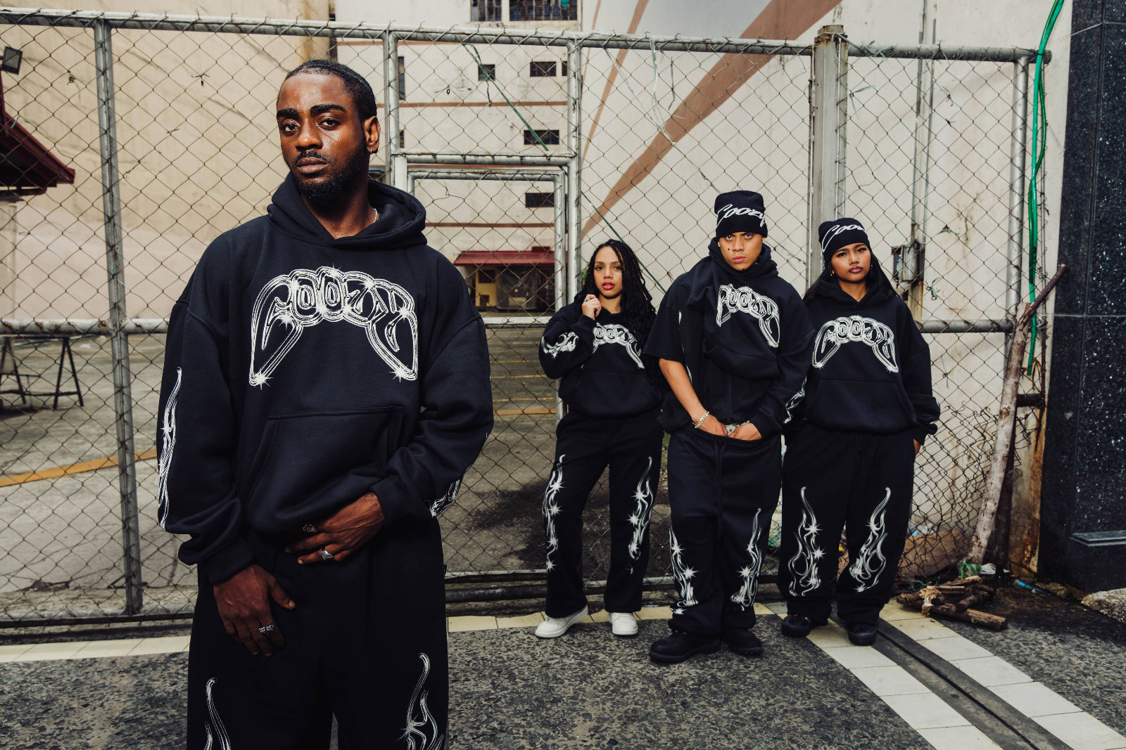 Four individuals wearing matching black outfits with a logo in an urban setting.