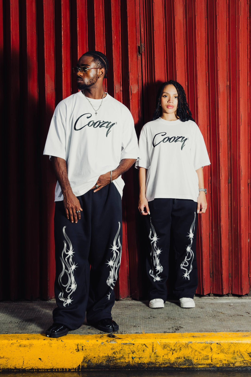 Two people wearing matching outfits with 'Cozy' branding in front of a red curtain.